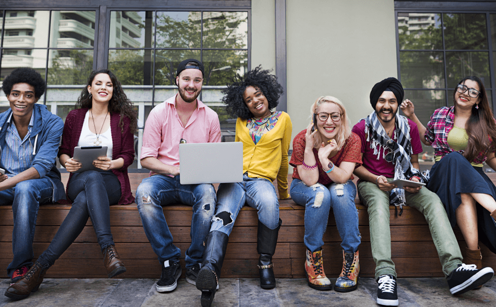 seven students smiling, sitting outside in a line