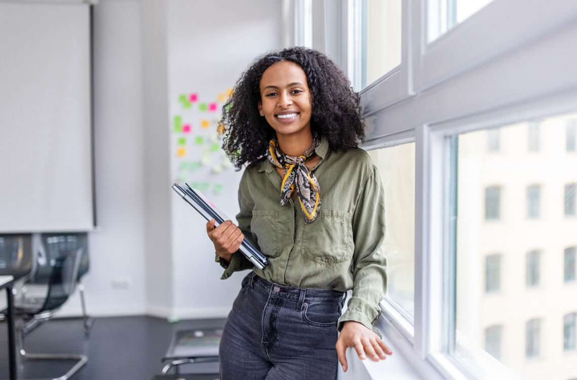 A young woman leaning against a window sill with notebooks in her hand ACAP Careers Academic Services