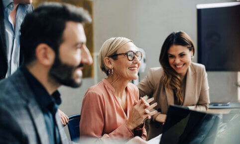 Two woman and two men smiling, working together on laptops in a classroom ACAP Careers MBA, coaching and IT