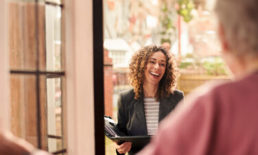 Smiling female social worker standing at the doorway of a client with a folder in hand