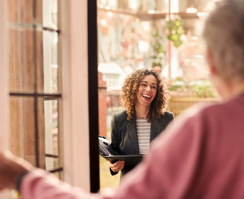 Smiling female social worker standing at the doorway of a client with a folder in hand