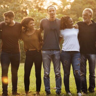 A group of people stand in a park, arm in arm, at dawn.