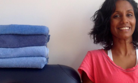 woman in pink top smiles next to massage table