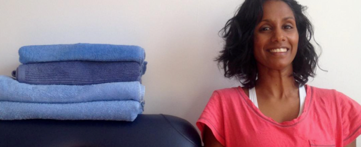 woman in pink top smiles next to massage table