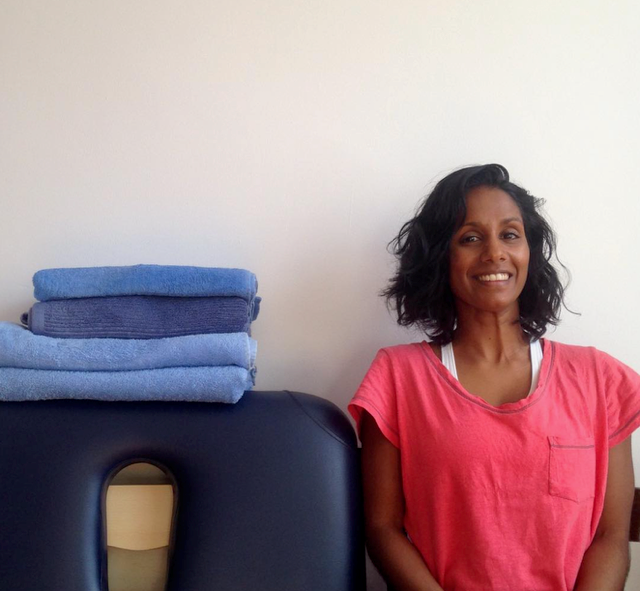 woman sits next to a massage tabke smiling wearing bright pink activewear