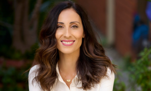 Woman with long brown hair and pink lipstick in a white collared shirt smiles at camera