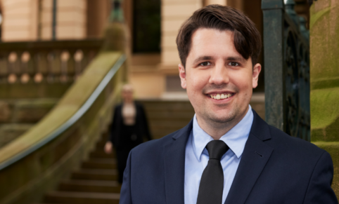 man in suit stands in front of sandstone building