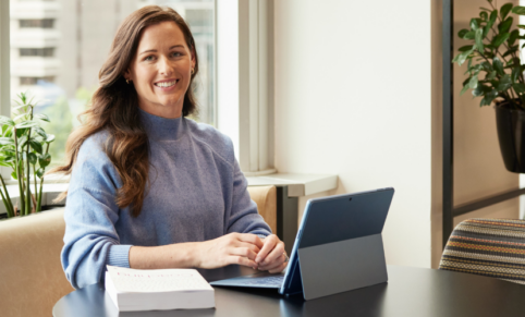 woman in blue jumper smiles at camera from laptop