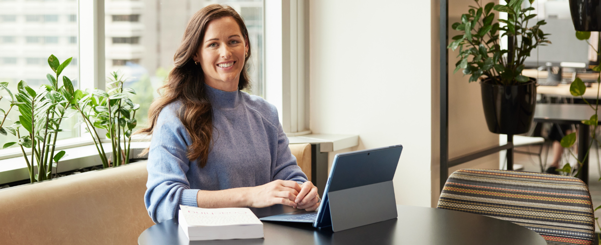 woman in blue jumper smiles at camera from laptop