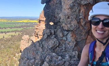 woman in climbing gear in front of rock with landscape in background