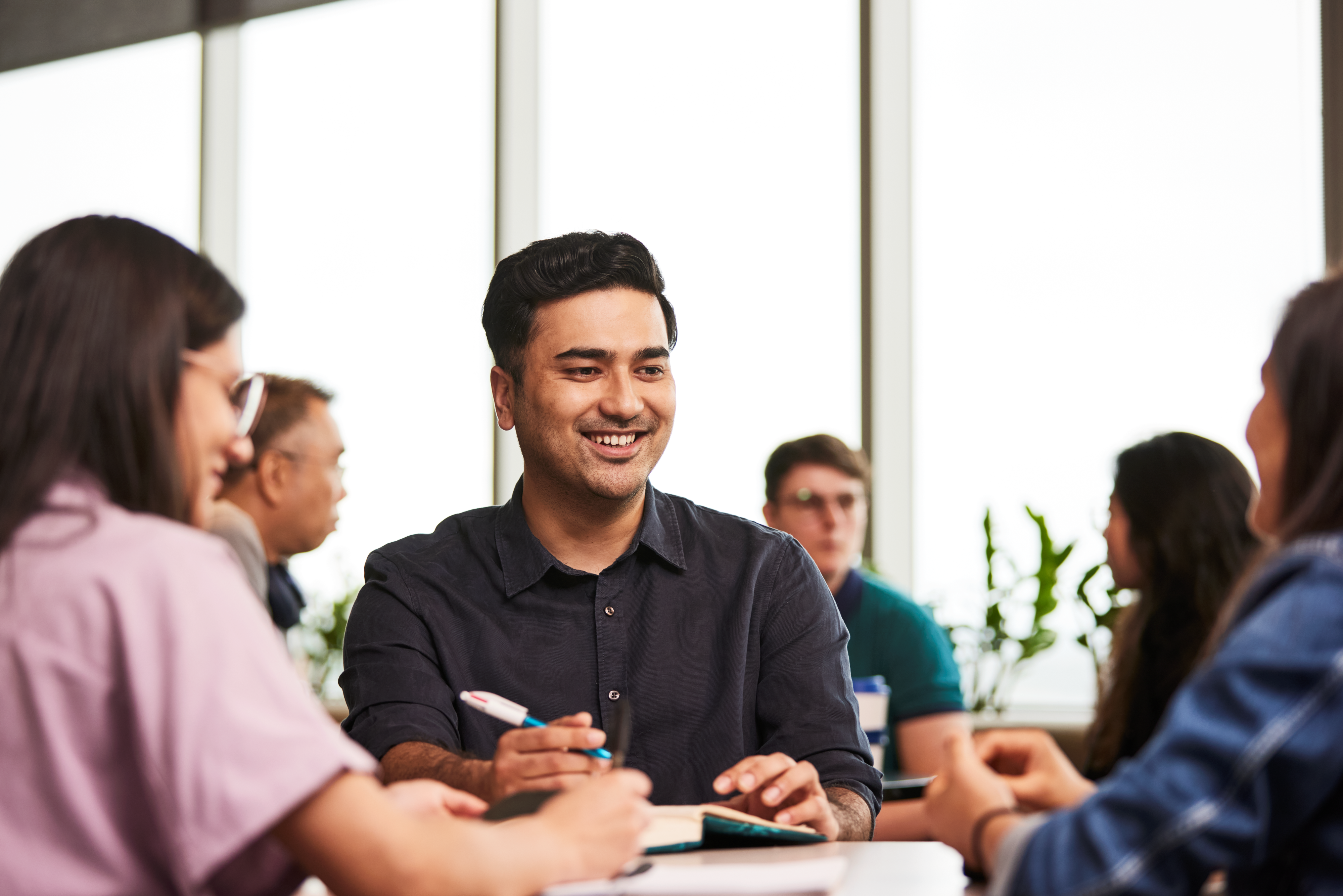 young man sits at study table smiling with other people