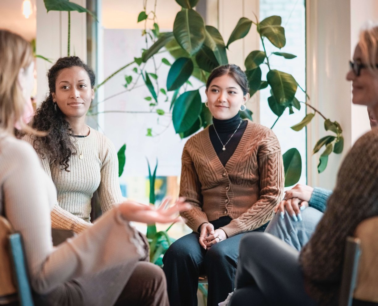 Four women sitting on chairs in a circle and talking to each other on campus