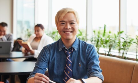 Photo of Psychology student and lecturer Tidus, sitting at ACAP Sydney campus and smiling to camera