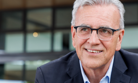 man with glasses and white hair looks into distance smiling in close up image