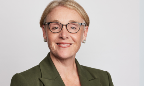 Woman with short blonde hair in glasses and green blazer in professional corporate headshot