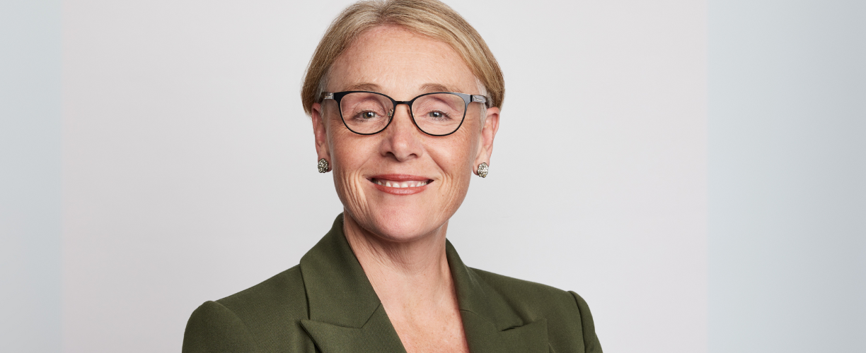 Woman with short blonde hair in glasses and green blazer in professional corporate headshot