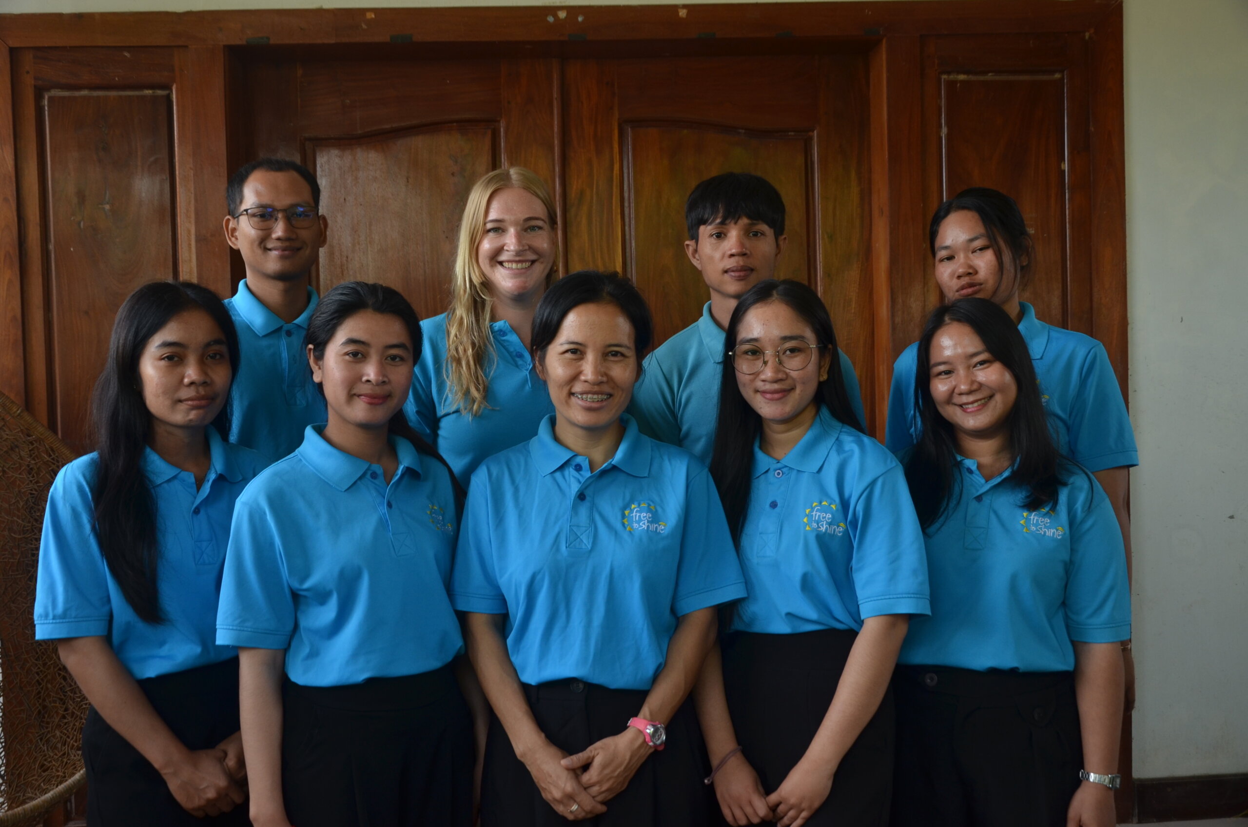 a group shot of people in blue polos all of Cambodian appearance except one woman with blonde hair in center